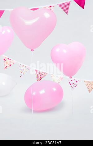 Palloncini da festa a forma di cuore rosa e bianco con tessuto rosa liscio e floreale Bunting Foto Stock