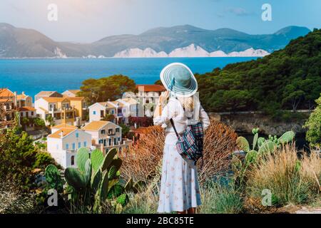 Foto d'epoca di donne turistiche che indossano cappello blu e zaino di viaggio godendo costa greca in piccola città di Assos. Cefalonia, Grecia. Foto Stock