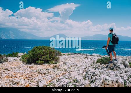 Turista maschile con macchina fotografica ammirando il paesaggio mozzafiato nuvola sulla catena montuosa sulla costa mediterranea del mare. Tramonto scena all'aperto di Ionian i Foto Stock