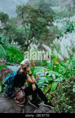 La ragazza riposa dopo aver tracciato la pietra e ammirando le spettacolari piante verdi di banana e canna da zucchero sulla valle. Isola di Santo Antao a Capo Verde. Vert Foto Stock