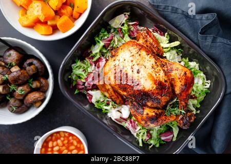 Tavolo con pollo intero arrosto, insalata, zucca, funghi, fagioli Foto Stock