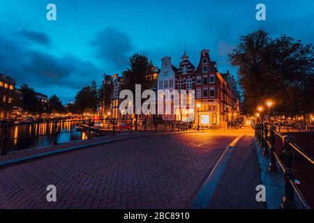 Ponte illuminato di Amsterdam con tipiche case olandesi di sera luci di ora blu, Olanda, Paesi Bassi. Foto Stock