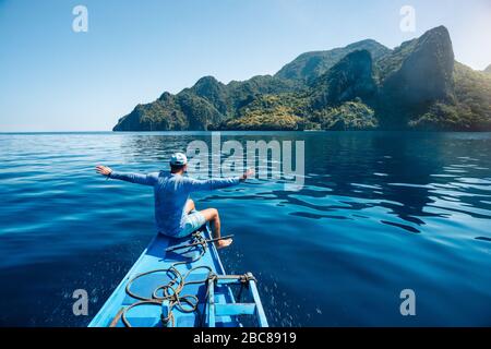 Vista posteriore dell'uomo sulla barca con diffusione di mani che arrivano all'esotica isola tropicale illuminato dalla luce del sole. Viaggi tour in Asia: El Nido, Palawan Phil Foto Stock