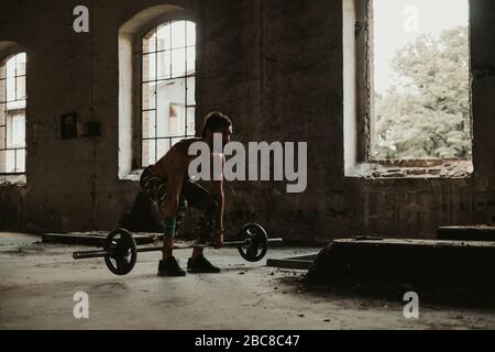 Uomo atletico barbuto che fa deadlift in un vecchio edificio. Bella giornata Foto Stock