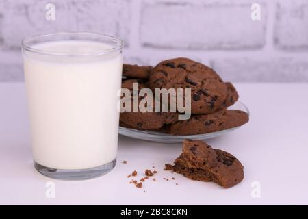 Bicchiere di latte e biscotti al cioccolato su sfondo bianco. Foto Stock