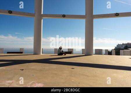 donna seduta a terra tra colonne e mare blu sullo sfondo Foto Stock