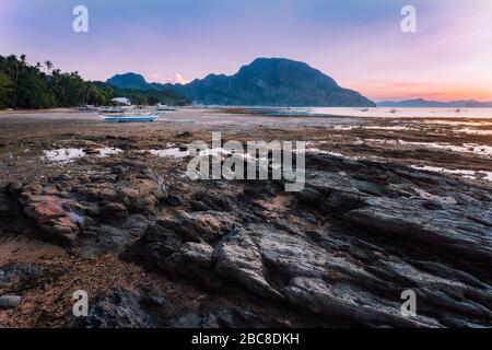 Villaggio di El Nido con le barche locali banca sulla riva illuminata dal tramonto a bassa marea. Pittoresco paesaggio naturale. Palawan, Filippine. Foto Stock