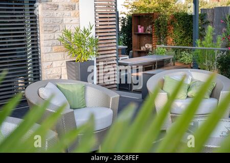 Mobili Garden lounge in rattan artificiale su una spaziosa terrazza con una facciata di palma sfocata in primo piano Foto Stock