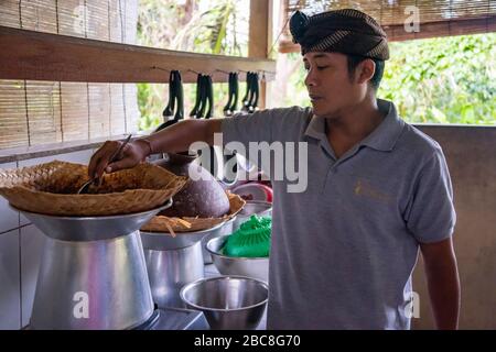 Ritratto orizzontale di un uomo che cucina riso il modo tradizionale a Bali, Indonesia. Foto Stock