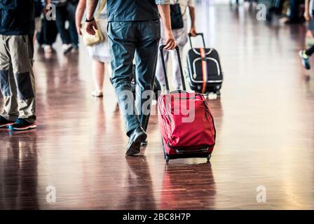 Viaggiatori con valigie che camminano attraverso l'aeroporto. Primo piano dei passeggeri che trasportano una valigia mentre camminano attraverso un ponte di imbarco per i passeggeri Foto Stock