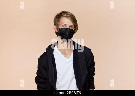 Ritratto di un giovane su sfondo caffè con maschera protegge contro il virus, maschera nera Foto Stock