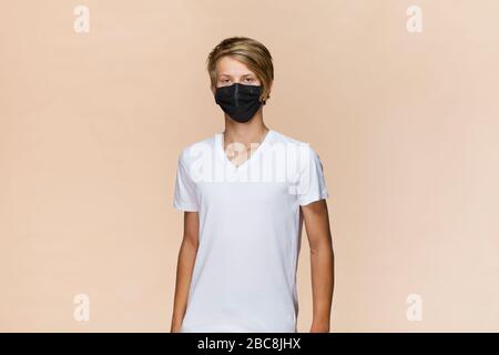 Uomo biondo con blusa nera e maschera facciale nera. Protezione da coronavirus. Foto Stock