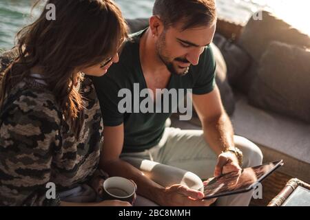 Buona coppia sorridente e guardando schermo tablet vicino al fiume in una giornata di sole Foto Stock