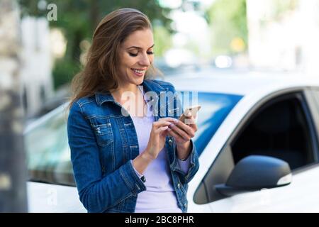 Donna che usa il telefono cellulare vicino all'auto Foto Stock