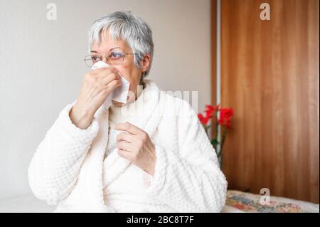 Pandemia di coronavirus. Salute, influenza, igiene e concetto di persone. Donna anziana malata con carta straccio che soffia il naso a casa . Foto Stock