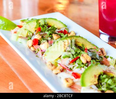 Tradizionale piatto di avocado ceviche messicano su una superficie di legno lucido chiaro in ristorante messicano con tradizionale bevanda di ibisco messicano Foto Stock