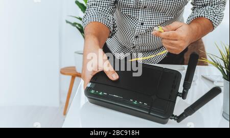 Cavo di rete mano e lan con le persone lavorano su router wireless, uomo che lavora da casa, mentre in quarantena durante la crisi di salute di Covid-19 Foto Stock