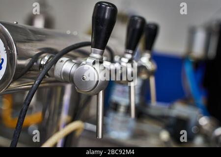 Attenzione selettiva al primo rubinetto di diversi rubinetti metallici con manici in gomma in fila collegati a macchine in una birreria Foto Stock