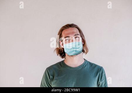 Giovane ragazzo che indossa maschera chirurgica viso, lungo capelli uomo prendere una maschera viso per coronavirus o COVID-19 epidemia Foto Stock