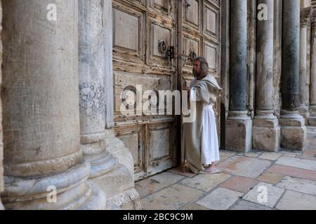 Un adoratore cristiano vestito come Gesù Cristo stare di fronte alla porta chiusa della Chiesa del Santo Sepolcro, in mezzo alla crisi pandemica Coronavirus COVID-19 nella vecchia città di Gerusalemme Israele Foto Stock