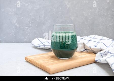 Frullato spirulina verde in una tazza di vetro su asse di legno su fondo grigio neutro con spazio per le copie Foto Stock