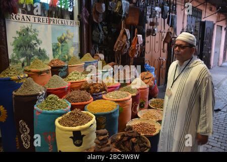 Una guida turistica si erge all'esterno di grandi botti di erbe secche e spezie presso il negozio di erbe tradizionali la Sagesse nel Souk Lekbir nella medina di Marrakech, Marocco. Foto Stock