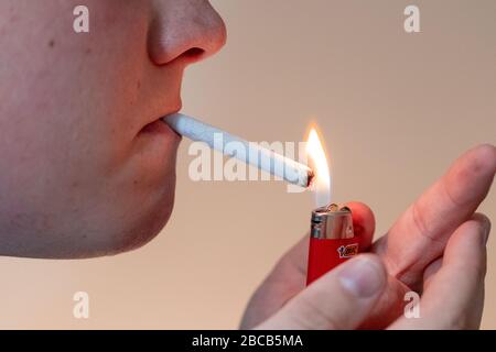 L'uomo illumina il giunto marijuana con l'accendisigari BIC rosso. Foto Stock