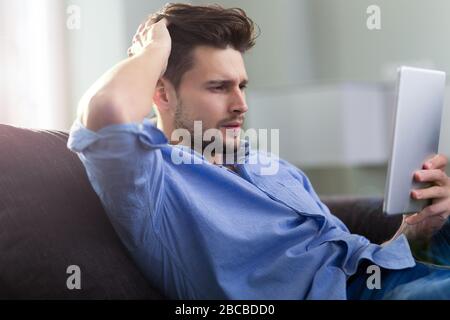 Uomo seduto sul divano con la tavoletta digitale Foto Stock