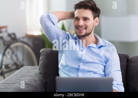 Uomo seduto sul divano con il computer portatile Foto Stock