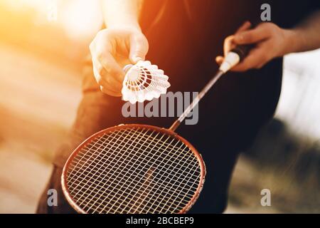 Un uomo sta tenendo una racchetta rossa di badminton e un shuttlecock bianco che sta andando essere gettato nell'aria in un giorno caldo e soleggiato. Foto Stock