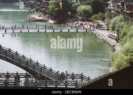 Feng Huang, Cina - Agosto 2019 : persone che attraversano pietre a passo sul fiume Tuo, che scorre attraverso il centro della città vecchia di Fenghuang Foto Stock