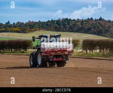 Trattore agricolo che sparge fertilizzante su un raccolto seminato su un giorno soleggiato di primavera, East Lothian, Scozia, Regno Unito Foto Stock