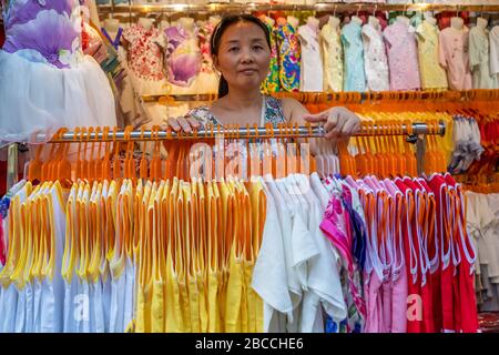 Chongqing, Cina - Agosto 2019 : Signora cinese in piedi dietro il rack con abiti da donna in vendita in negozio di tessuti in ci Qi Kou città antica Foto Stock