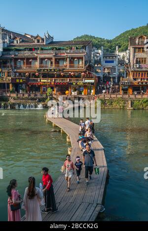 Feng Huang, Cina - Agosto 2019 : persone che attraversano l'acqua sul ponte di legno sentiero attraverso il fiume Tuo Jiang Tuojiang nella città vecchia di Fenghuang conosciuto Foto Stock