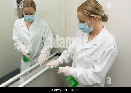 Donna che usa una salvietta bagnata e uno spray igienizzante imbevuto di alcool per pulire la ringhiera nell'ascensore. Disinfezione, pulizia e assistenza sanitaria, Anti Coronavirus COVID Foto Stock