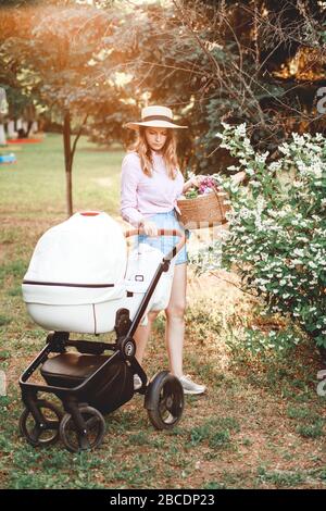 Una donna sta camminando con un passeggino sul sentiero nel parco al tramonto. Si chinò al bambino nel passeggino Foto Stock