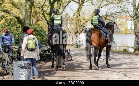 Amburgo, Germania. 04th Apr, 2020. I poliziotti montati fanno notare a persone in un parco sull'Alster esterno che, come parte del divieto di contatto per contenere il coronavirus, è vietato sedersi all'esterno su prati o panchine. Credito: Markus Scholz/dpa/Alamy Live News Foto Stock