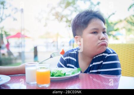 Obesi Fat Boy con espressione di disgusto contro le verdure in insalata, rifiutando il concetto di cibo Foto Stock