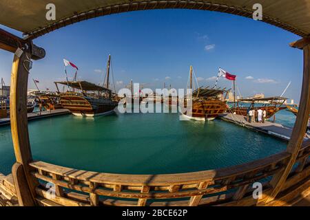 Tradizionali barche in legno (dhows) a Katara spiaggia Qatar vista luce del giorno con bandiera Qatar e nuvole nel cielo Foto Stock