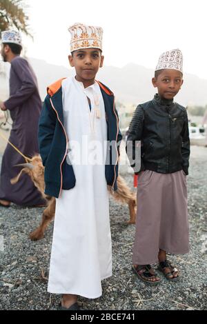 Bambini e giovani uomini vestiti elegantemente lavorando al mercato del bestiame settimanale del venerdì a Nizwa, Oman Foto Stock