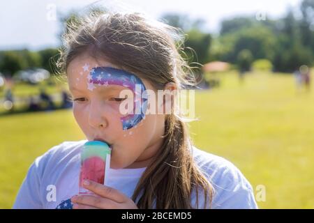 Teenager con la vernice del viso che mangia il gelato di colore della ciotola della pioggia. Foto Stock