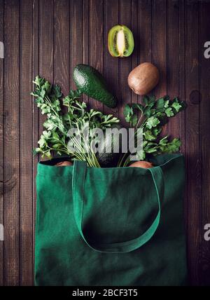 Consegna online degli acquisti. Borsa ecologica con avocado, kiwi e verde su sfondo marrone in legno Foto Stock