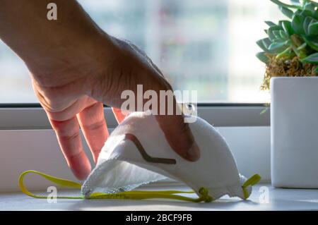 Una mano maschile sta raccogliendo una maschera facciale N95 su un banco. Foto Stock