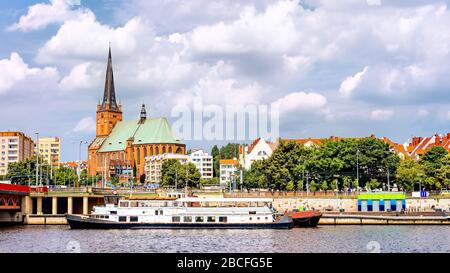 Navi ancorate al molo del fiume Odra. Persone che si rilassano su Piastowski Boulevard. Cattedrale Basilica di San Giacomo Apostolo sullo sfondo, Szczecin, Polonia Foto Stock