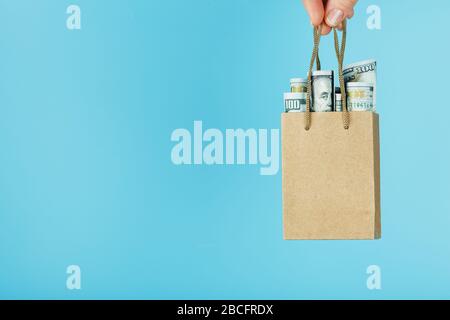 Un piccolo sacchetto di aiuto fatto di carta in una mano tesa con dollari USA su uno sfondo blu. Disposizione dei modelli di imballaggio con spazio per la copia, pubblicità Foto Stock