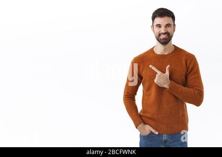 Bell'uomo bearded, proprietario dell'azienda che invita a sostenere il suo start-up, puntando il dito a sinistra, mostrando informazioni o banner di prodotto pubblicità, sorridendo compiaciuto Foto Stock