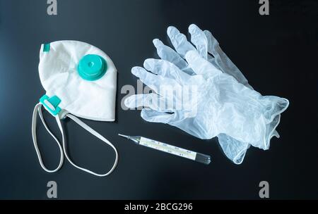 Guanti, maschera e termometro su sfondo nero. Soggetti medici per il trattamento del virus Foto Stock