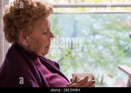 Donna anziana seduta accanto alla finestra Foto Stock
