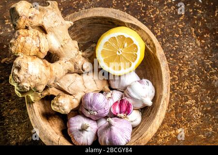 Le garlicci, un limone e uno zenzero si trovano in un piatto su un tavolo di legno. Gli alimenti migliori per amplificare il vostro sistema immune Foto Stock