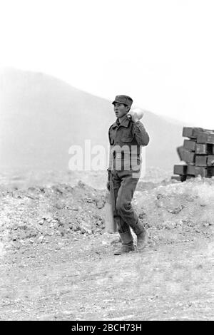 Un soldato afghano porta i colpi di artiglieria per un cannone 122mm costruito in Unione Sovietica al Pagaman, posto operativo in avanti il 1° maggio 1989 a Pagaman, Afghanistan. La base protegge un punto di ingresso principale nella capitale Kabul e si trova a meno di un chilometro e mezzo dalle linee frontali dei combattenti afghani mujahideen. Foto Stock